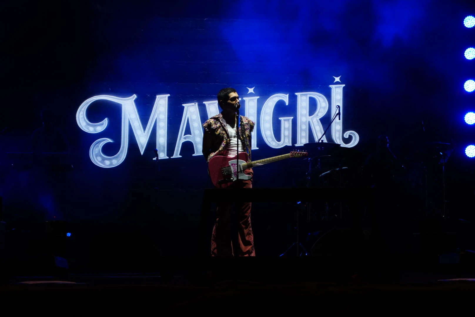 Mavi ışıklar ve Mavi Gri yazısı önünde gitar çalan vokalist