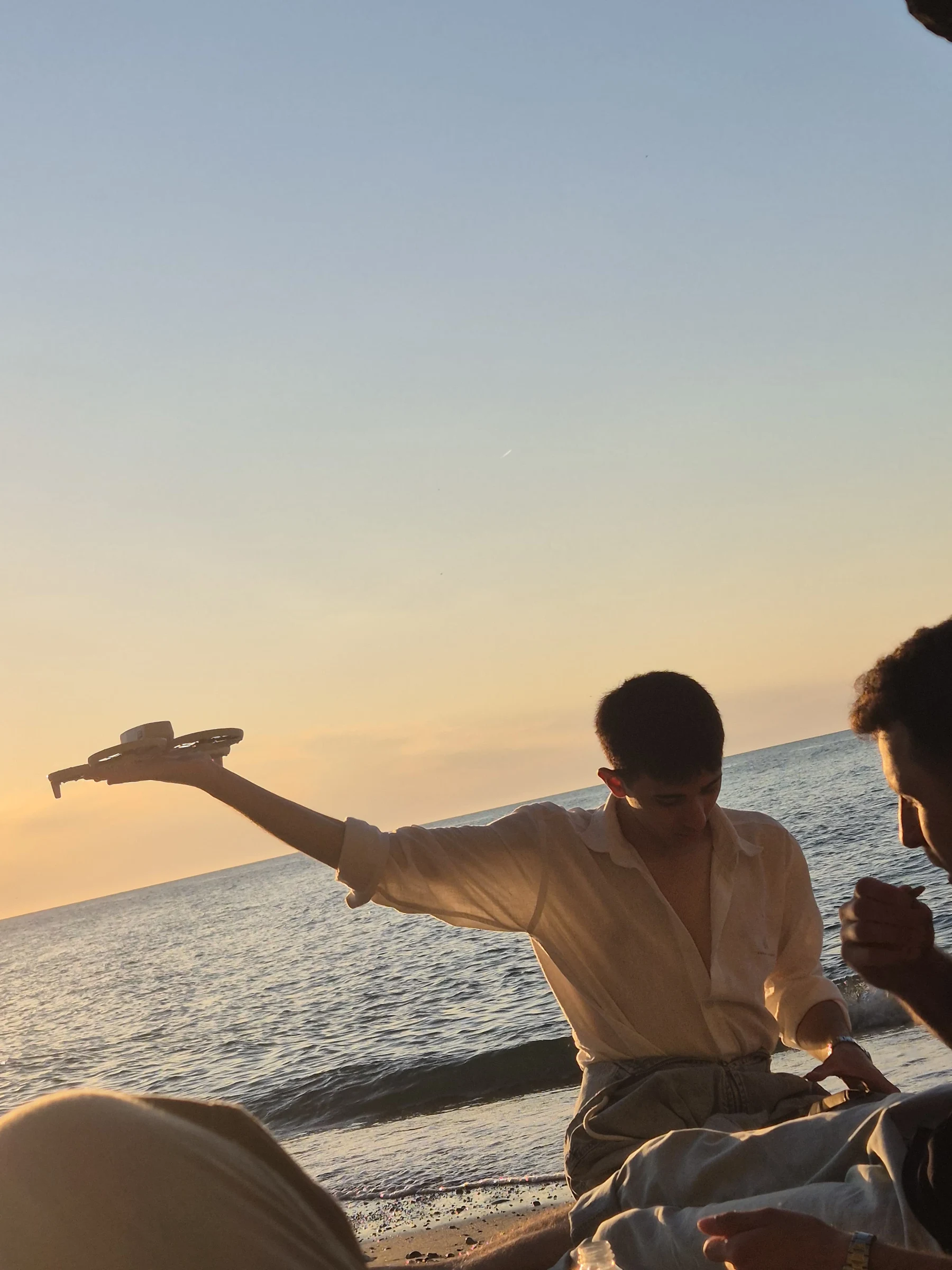 Gün batımında sahilde elinde drone tutan Eren